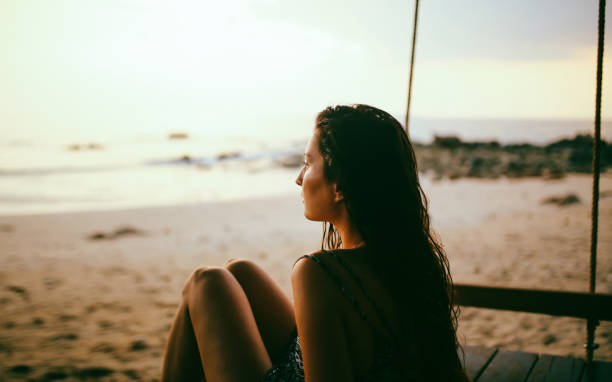 volta iluminado retrato de uma jovem mulher na praia, apreciando o pôr do sol - life back lit people happiness - fotografias e filmes do acervo