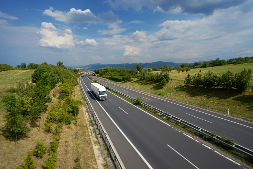 White truck driving on a highway in a rural landscape with ecoduct, city and mountains in the background. View from above.