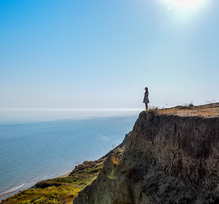 The girl is standing on a cliff near the sea.