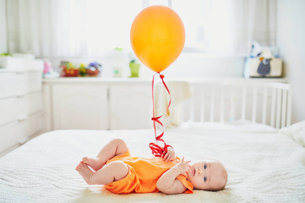Adorable baby girl in orange romper suit with colorful balloon stock photo