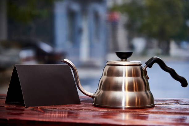 A kettle and a black empty booklet stand on a wooden table on a blurred background