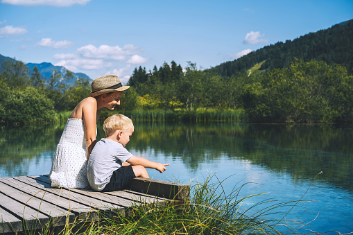 Mother and son on wooden bridge on nature background of lake and mountains. Travel, Family, Lifestyle concept. Parent and child together. Zelenci natural reserve near Kranjska Gora, Slovenia, Europe.