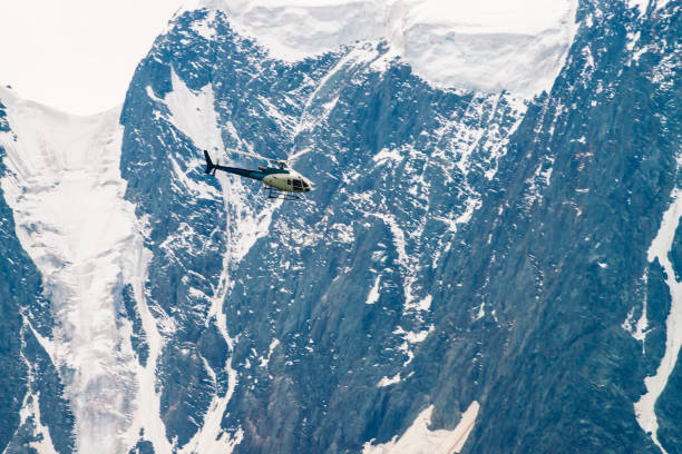 Helicopter in air against background of snowy mountain. Rescue mission in glaciers to rescue climbers. Aerial tourism in highlands in overcast weather. Atmospheric view on icy rock close up. Helicopter in air against background of snowy mountain. Rescue mission in glaciers to rescue climbers. Aerial tourism in highlands in overcast weather. Atmospheric view on icy rock close up. altay state nature reserve stock pictures, royalty-free photos & images