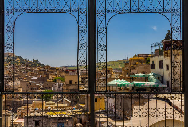 View of ancient rooftops of the Fez medina through an ornate metal window frame View over the ancient yellow clay rooftops of the Fes medina through an ornate metal window frame marrakesh riad stock pictures, royalty-free photos & images