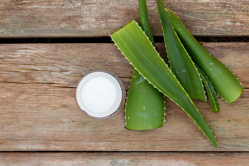Green leaves of aloe vera plant and moisturizing cream on rustic wooden background