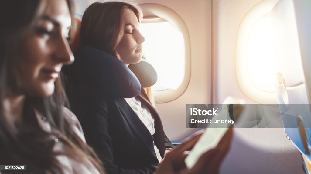 Two females going on business trip by plane. A woman reading an e-book on a smartphone Two females going on business trip by plane. A woman reading an e-book on a smartphone. Airplane Stock Photo