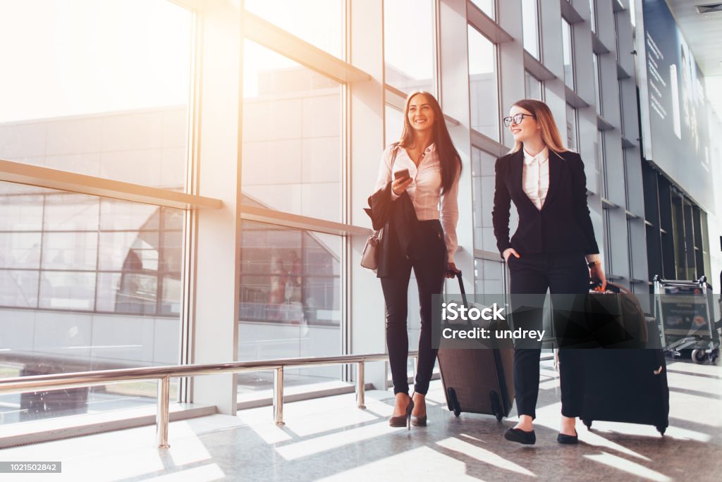 Dos sonrientes a socios en negocios viaje maletas transporte mientras camina por el pasillo del aeropuerto - Foto de stock de Aeropuerto libre de derechos