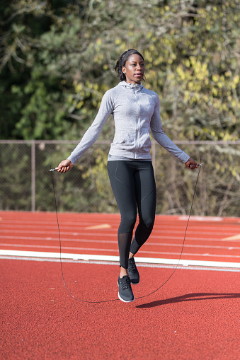 An African American female track athlete gets warmed up by jumping rope on the track.