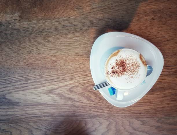 White cup of caramel coffee on black table for charge energy, refresh, breakfast or breaking time in afternoon. Cappuccino hot coffee on top with foam milk and caramel cream.