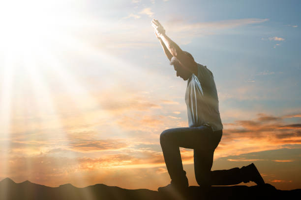 mann kniet und betet bei sonnenuntergang - praying men god kneeling stock-fotos und bilder