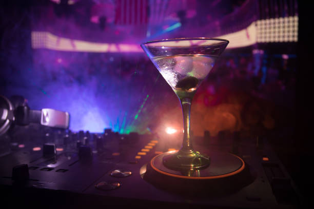 istock Glass with martini with olive inside on dj controller in night club. Dj Console with club drink at music party in nightclub with disco lights. Close up view 1021557280