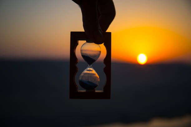 istock Life time passing concept. Hand holding hourglass with sunset sky background. 1021557432