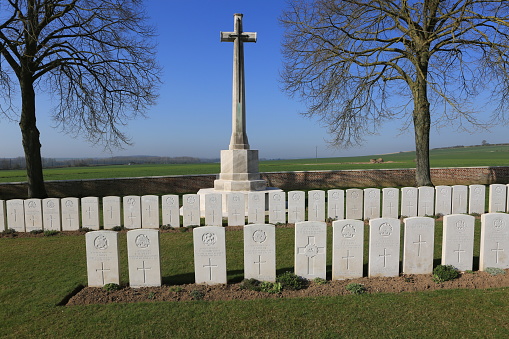 The Cross of Sacrifice in WW1 cemetery in the Somme region of France. The cross has an inverted sword in the middle, and there are graves in two rows infant of the cross.