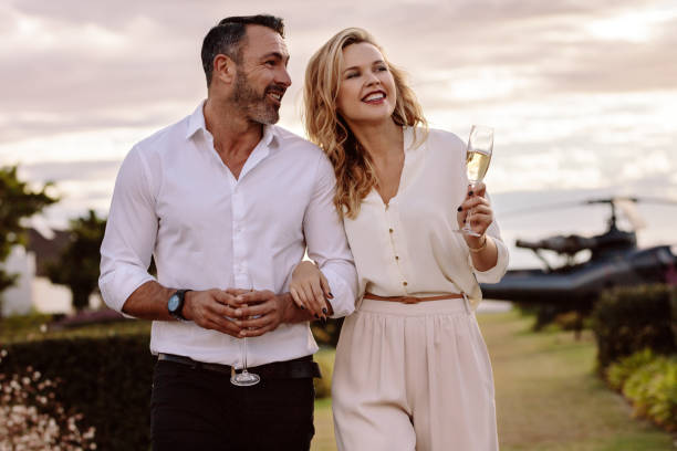 Elegant couple walking outdoors with wine Handsome man with his beautiful girlfriend walking together outdoors. Beautiful couple walking outdoors with a helicopter at the back. wealthy lifestyle stock pictures, royalty-free photos & images