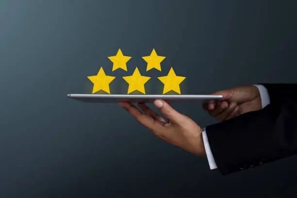 Photo of Customer Experience Concept. Businessman Holding a digital tablet to Present Five Star Rating on Satisfaction Survey, Side view, Dark tone