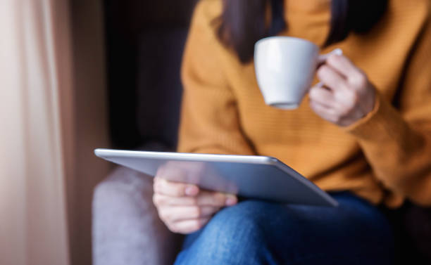 istock Reading Concept. Young Woman using Tablet  and Drinking Coffee. Relaxing in Cozy House, Sit on the Chair, Front View and Selective Focus 1021563444