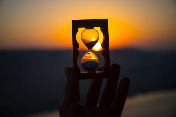 istock Life time passing concept. Hand holding hourglass with sunset sky background. 1021568406