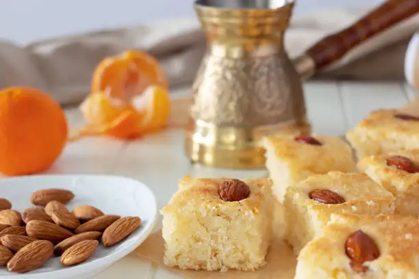 Photo of Still life Pieces Basbousa or namoora traditional arabic dessert. Semolina cake with almond nut and syrup, orange and cooper jezva. Copy space. Selective focus.