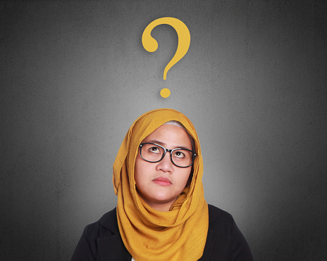 Asian muslimah businesswomen wearing glasses with curiosity expression and a question sign above her head. Isolated on gray. Close up head and shoulders