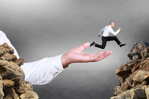 Composite image. Businessman running jumping trough obstacle gap with the help of big leader hand