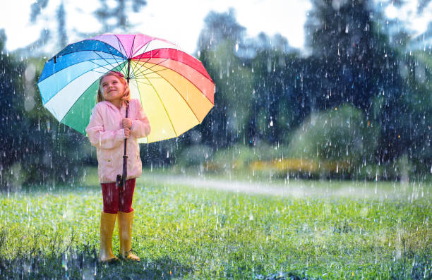 glückliches kind mit regenbogen regenschirm unter regen - regen stock-fotos und bilder