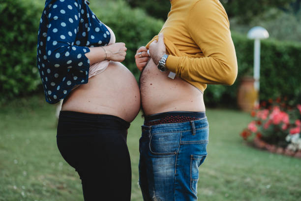 Young adult couple in love joking together Young adult couple in love joking together. She's pregnant and and he too pretends to be pregnant. human abdomen photos stock pictures, royalty-free photos & images