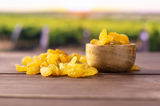 Lot of whole dry golden raisins sultana variety with wooden bowl with vineyard in background