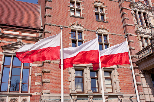 Three Polish flags waving on the wind with red bricks building in background