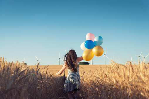 Girl with colorful balloons is running the way to wind energy - Wind energy concept
