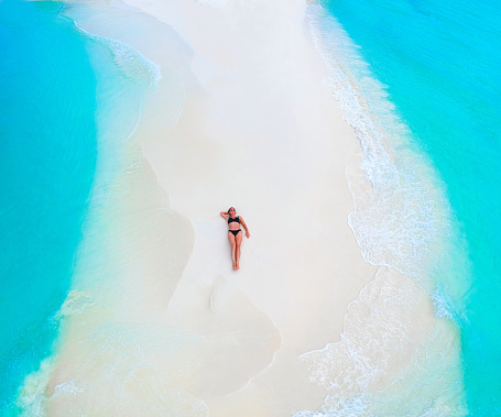 Beautiful woman tans on sandbank surrounded by turquoise ocean from above