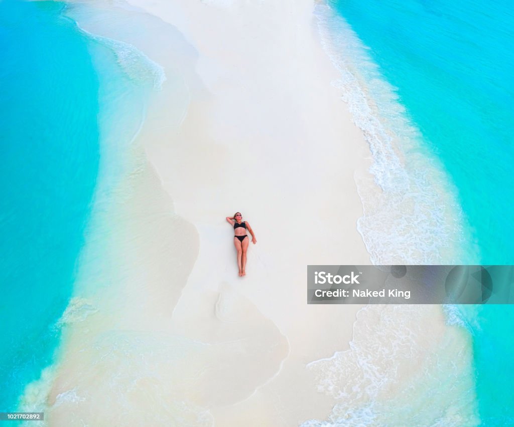 Beautiful woman tans on sandbank surrounded by turquoise ocean from above Beach Stock Photo