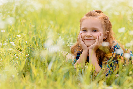 portrait of little smiling child resting on green grass in meadow