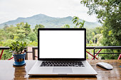 blank screen of laptop with mouse and  plant vase on wooden table, Mountain and forest background