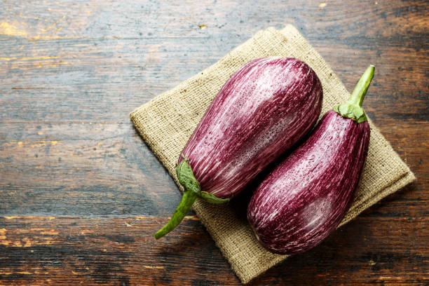 istock two ripe motley eggplants on a wooden table, lying on burlap. 1021734782