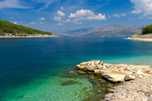 Sunny summer day on the Croatian beach in Pucisca, Dalmatia, island of Brac.
Clear bay with blue water, rocks and stones and view of the croatian coastline with mountains.
Summer travel destination.