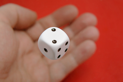 The dice shows two and is above the hand blurred on a red background.