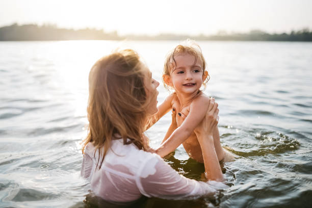 istock mother holding happy daughter in river during sunset 1021782676