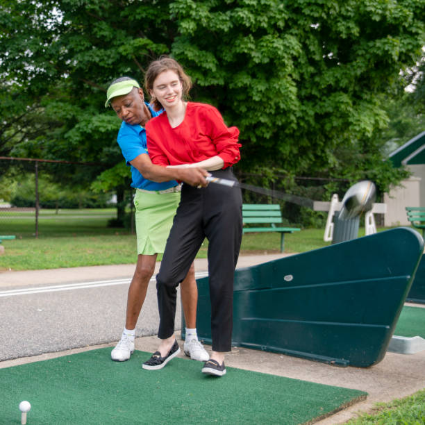 the active 77-years-old senior african-american woman teaching the 18-years-old caucasian girl to play golf. - golf golf swing putting cheerful imagens e fotografias de stock