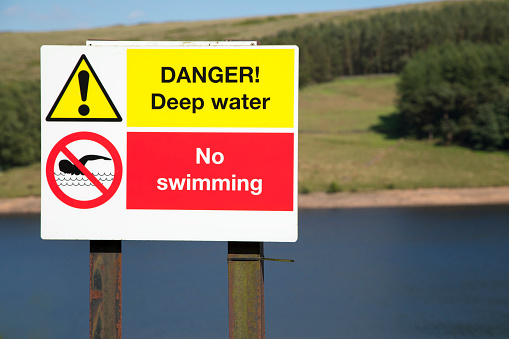 A red and white no swimming, deep water sign next to a body of water