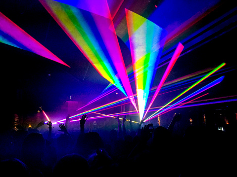 Colourful neon laser lights in a nightclub with silhouette of people.