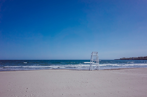 An empty lifeguard chair on a beach facing the ocean