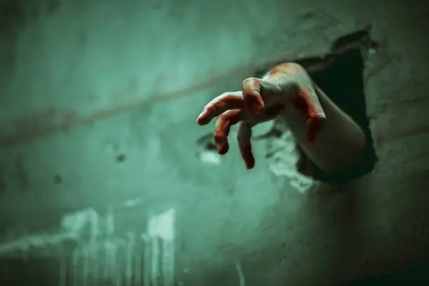 Photo of Zombie hand through the cracked wall. Horror and scary film concept. Halloween day theme. Green tone like ghost movie