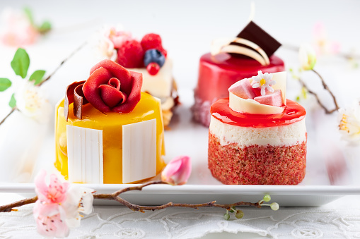 Various mini cakes on a white plate. Sweets decorated with fresh berries and flowers for holiday.