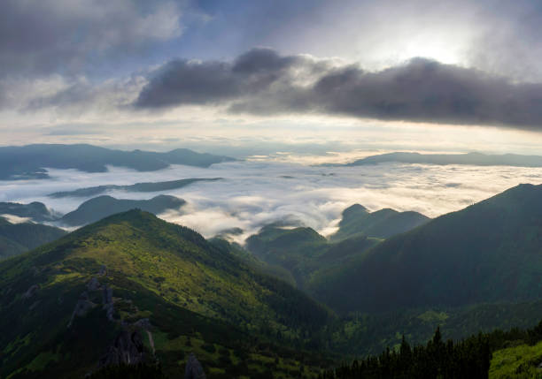 istock Fantastic view of mountain valley covered with low white puffy like snow clouds stretching to foggy horizon under bright morning sky with light orange glow at sunrise. Beauty of nature concept. 1021853614