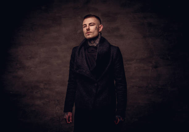Tattoed young guy in a black jacket posing at the studio. Isolated on a dark textured background.