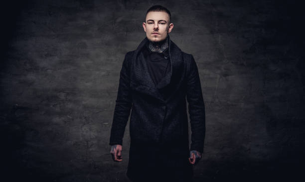istock Tattoed young guy in a black jacket posing at the studio. Isolated on dark textured background. 1021859502