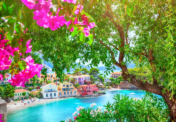 Panoramic view to Assos village Kefalonia. Greece. White lonely yacht in beautiful turquoise colored bay lagoon water surrounded by pine and cypress trees along the coastline.
