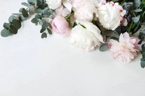 Styled stock photo. Decorative still life floral composition. Wedding or birthday bouquet of pink and white peony flowers and eucalyptus branches, white table background. Flat lay, top view.