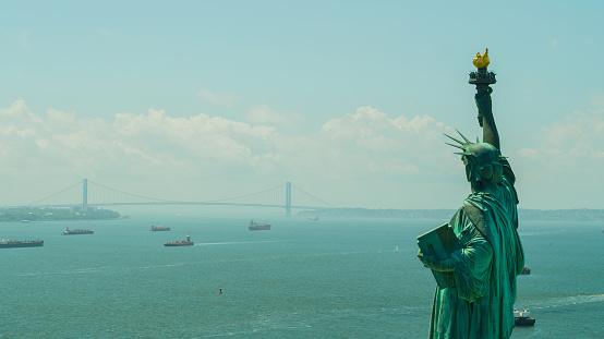 Aerial drone image of the Statue of Liberty overlooking harbor water with ships