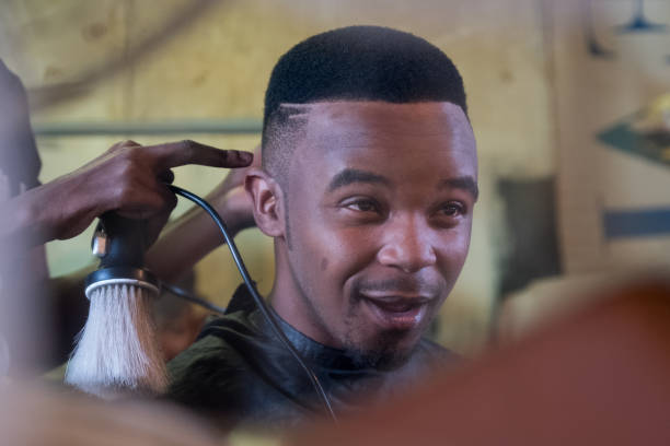 Enjoying my haircut at the local township barber A young black male has his hair cut at the local barber shop in the township in Cape Town, South Africa black barber stock pictures, royalty-free photos & images